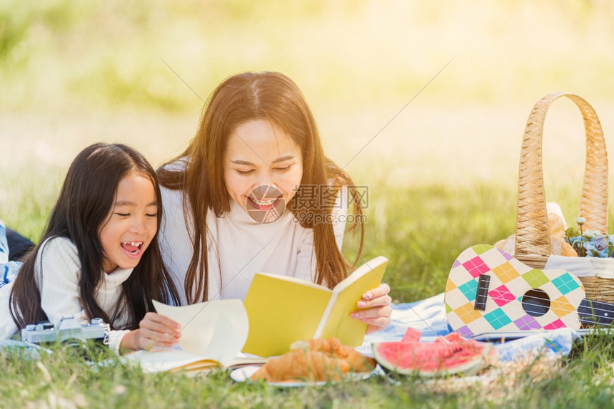 快乐的亚洲年轻家庭母亲和小女孩在户外享受乐趣和在夏季花园春野餐毯子阅读书家庭放松概念上躺在野餐毯子图片