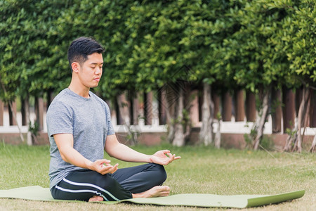亚洲青年男子在室外用冥想莲花做瑜伽坐在绿草上花园公闭眼健康保概念图片
