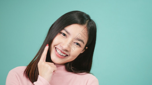 青春的亚洲年轻美女微笑着在蓝色背景孤立的牙齿上佩戴硅酮或口服牙膏用可移动的牙套后保留工具图片