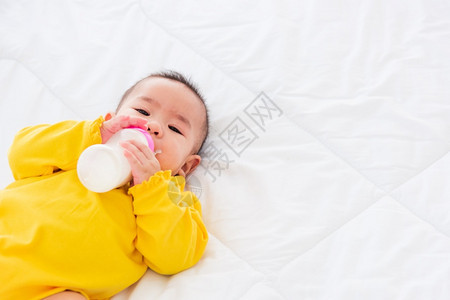 婴儿躺床上拿着一瓶牛奶喝图片