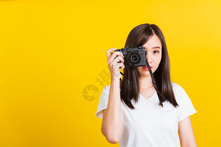 快乐的亚洲美丽年轻女摄影师的肖像正在拍照取景器上的复古数码无镜相机准备拍摄摄影棚拍摄的黄色背景上孤立图片