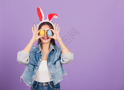 紫背景戴兔耳朵和手拿彩色鸡蛋微笑的女士图片