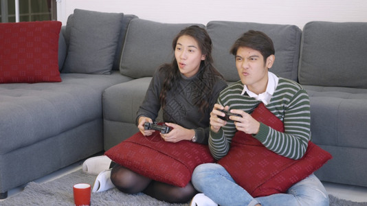 快乐的亚洲美丽的年轻家庭夫妇夫妻笑嘻嘻的玩着游戏机拿着游戏机快乐和游戏的概念图片