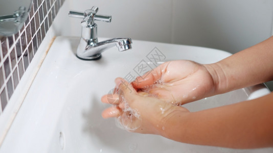 利用肥皂和在水龙头下洗手来拉紧年轻女手在旅馆浴室水槽中用白色泡在洗手池中以保护她免受新冠的伤害图片
