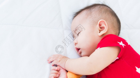 美丽的亚洲新生儿小宝在家中睡白床上快乐宝穿着红衬衫在房间里放松枕头图片