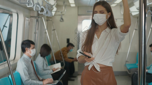 在地铁列车旅行中使用智能手机站立的白种人年轻女在火车上用手机监听音乐图片