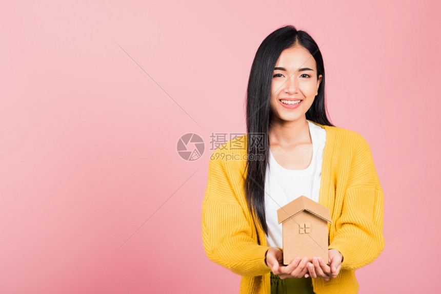 快乐的亚洲肖像美丽可爱的年轻女子兴奋的笑着手持有房屋模型工作室拍摄孤立在粉红背景上代理女持有家庭房地产保险和银行业概念图片
