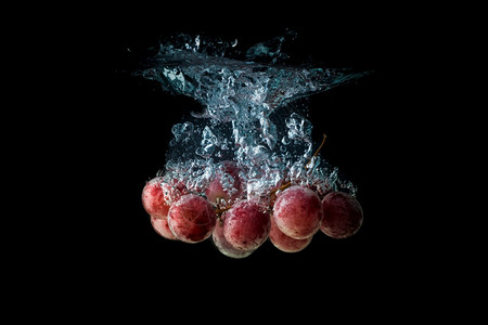 红葡萄喷洒和沉入水中在黑色背景与气泡图片