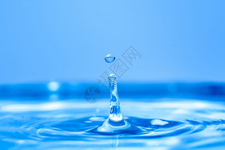水滴落到晶清晰的蓝中产生波纹背景图片
