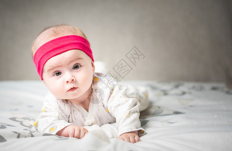 6个月大的婴儿睡在肚子上的床头抬起用大眼睛看相机自然卧室灯光6个月大的婴儿睡在肚子上的床用大眼睛看相机自然光图片