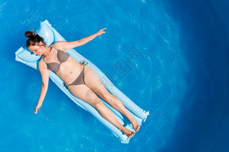 穿着比基尼的年轻女子在空中马特瑞斯环绕地面游泳池顶层风景家庭节日概念空中马特瑞斯的比基尼年轻女子在地面游泳池图片