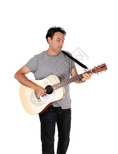 一个年轻的英俊男子站在他的吉手旁边弹着歌唱牛仔裤和T恤图片