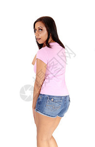 一位年轻美女站在工作室穿着牛仔裤短和山顶粉刺肩上看膀与白种背景隔绝图片