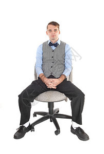 一个穿着衣服裤子的英俊年轻男穿着灰色背心蓝衬衣坐在办公室椅子上图片