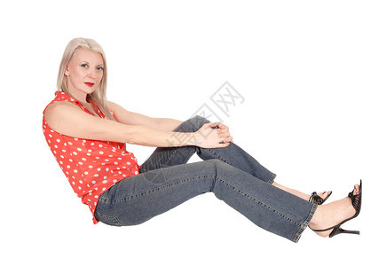 一个中年金发美女坐在工作室里穿着牛仔裤穿着上衣放松与白背景隔绝图片