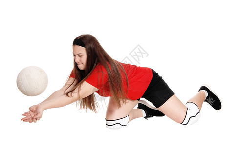 一个十几岁的女孩穿着制服打排球跪在膝上试图抓住球与白种背景隔绝图片