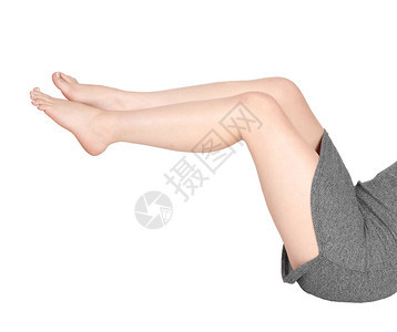身穿短灰色裙子躺在地板上赤脚抬起双腿因白色背景被隔离图片