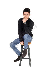 穿着黑色毛衣和牛仔裤的美丽青年男子坐在酒吧椅上一手双在下巴因白背景被隔离图片