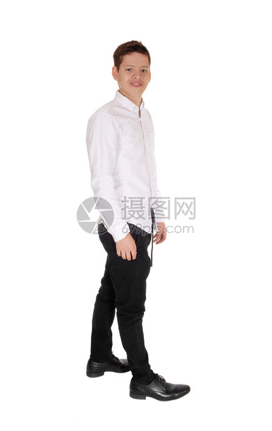 一个快乐的少年男孩站在白衬衫和黑裤子上被白色背景隔离看着摄像机图片