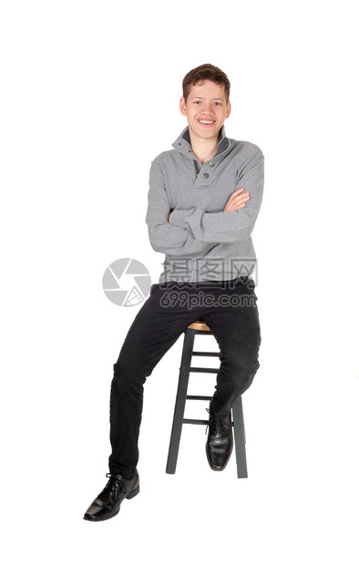 一个年轻男孩坐在灰色的毛衣里手与在椅子上笑与白背景隔绝图片