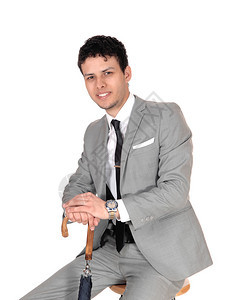 一个穿着浅灰色西装的年轻男子坐在一个工作室白背景手放在雨伞上微笑图片
