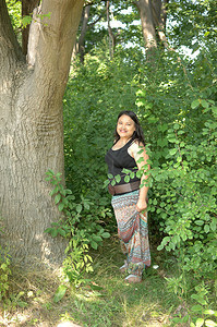 可爱的年轻姑娘穿着长裙站在森林里阳光灿烂的大树上微笑着图片
