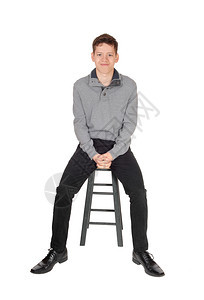 一个年轻男孩坐在灰色的毛衣里手折在椅子上笑着的手折在椅子上为白色背景而孤立图片