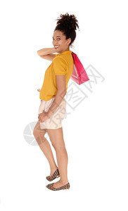 一个美丽的笑着容多种族妇女穿着黄色的毛衣和短裤站在肩膀上拿着一个购物袋被隔离在白地上图片
