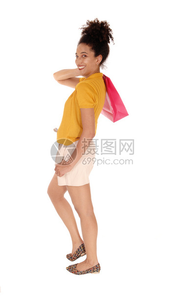 一个美丽的笑着容多种族妇女穿着黄色的毛衣和短裤站在肩膀上拿着一个购物袋被隔离在白地上图片