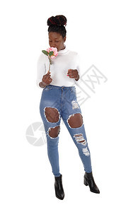 一个高的非裔美国女青年穿着破烂牛仔裤闻着粉红玫瑰的香味与白种背景隔绝图片