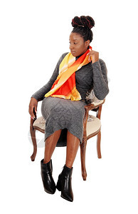 一个穿着长灰色裙的华丽非裔美国妇女坐在一把旧扶手椅上被白背景隔离图片