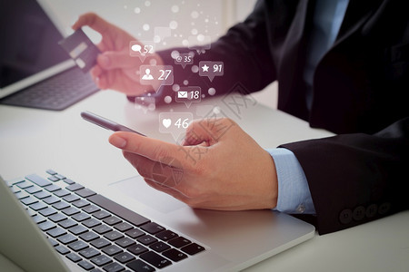 商人在网上购买信用卡在现代服务台用移动电话和笔记本脑购买信用卡图片