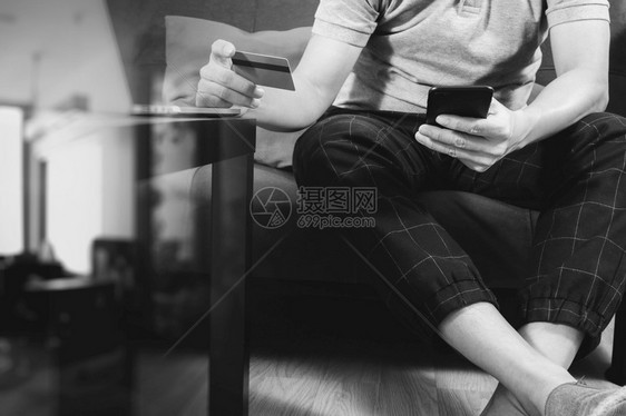 使用智能电话和膝上型计算机数字平板对接键盘持有网上信用卡付款坐在客厅沙发上家工作概念黑白图片