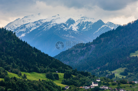 夏季阿尔卑斯山地景观与村庄山坡上的森林和远在奥地利的冰雪覆盖了岩石顶峰图片