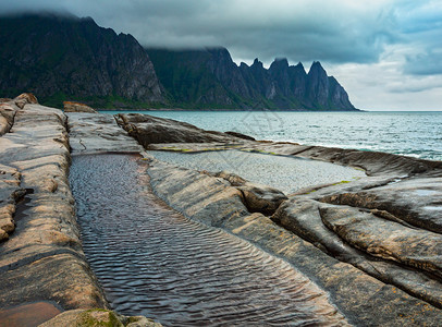 挪威Senja市Ersfjord的沙滩上有潮汐浴夏季极地日夜海岸远处的龙牙岩图片