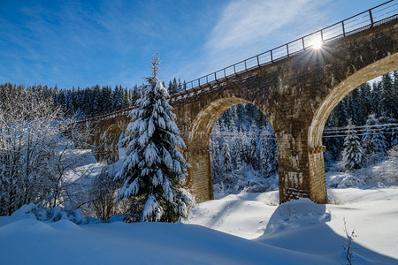 在山雪森林的铁路上建造石桥archbridge雪漂在路边树木和电线上漂浮背景图片