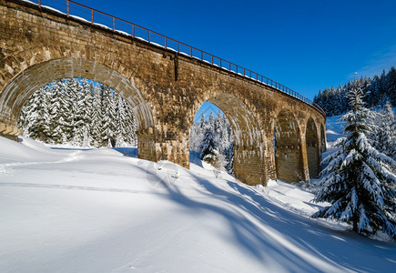 在山雪森林的铁路上建造石桥archbridge雪漂在路边树木和电线上漂浮图片