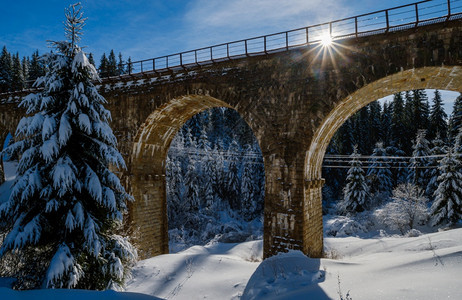 在山雪森林的铁路上建造石桥archbridge雪漂在路边树木和电线上漂浮背景图片