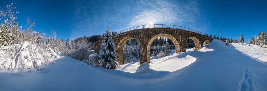 铁道上的石桥archbridge穿过山雪森林漂浮在路边树木和天空的阳光飘浮在冰霜中背景图片