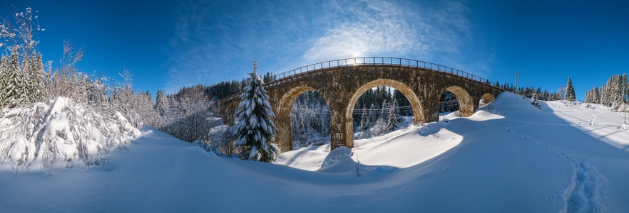 铁道上的石桥archbridge穿过山雪森林漂浮在路边树木和天空的阳光飘浮在冰霜中图片