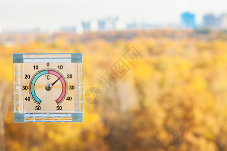在阳光温暖的秋天家庭窗户的外温度计和在阳光暖的秋天背景上模糊的黄色城市公园图片