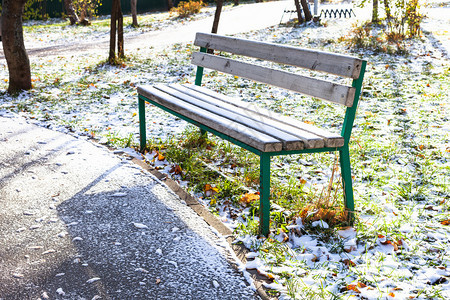 城市花园中靠近人行道的空凳子秋天寒冷的第一场雪覆盖着城市花园中的第一个雪图片