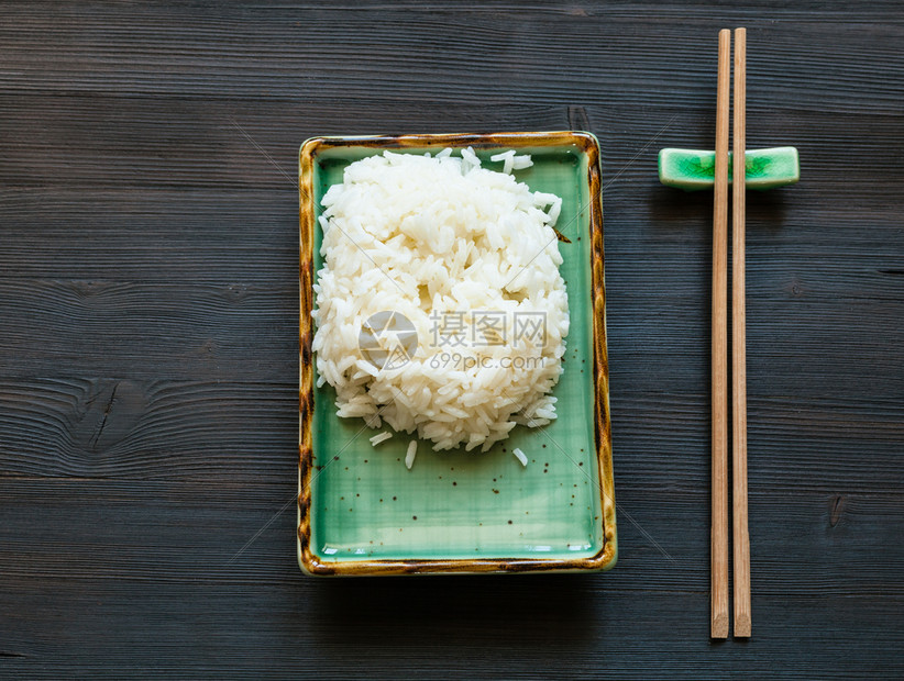 绿色盘子上煮熟米和棕色桌上用复印空间休息的筷子顶部视图图片