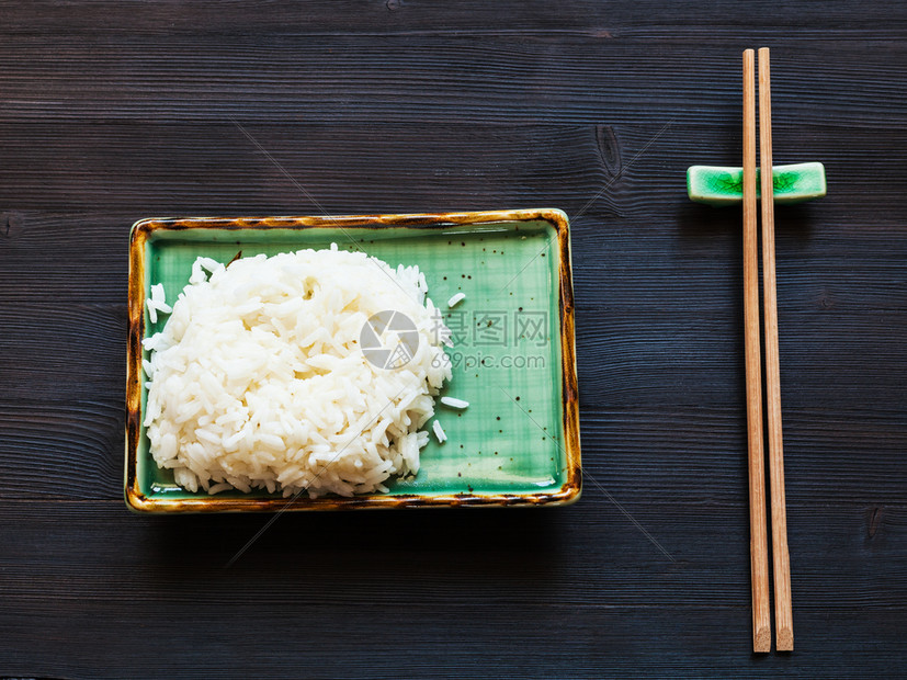 绿板上部分煮饭和深棕桌上休息的木筷子图片