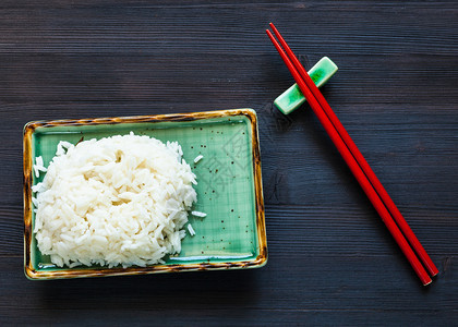 绿板上部分煮饭米和黑木板上休息的红筷子图片