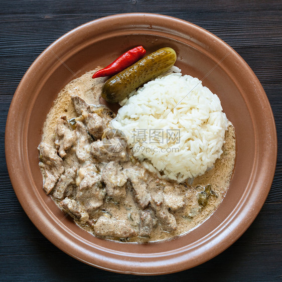 俄罗斯料理棕色盘子里放着牛肉斯特罗加诺夫BeefStroganovBefstroganov酸奶油炖肉和煮米饭深色木板图片