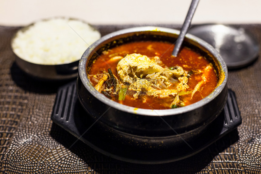 Korean烹饪yukgaejang当地餐馆用勺子装有牛肉鸡蛋蘑菇淀粉面扇菜ferns豆芽煮饭的热辣汤和的金属碗图片