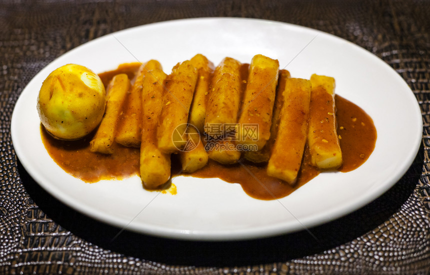 当地餐厅黑棕色皮巾板上白的盘子Tteokbokki零食加辣酱鸡蛋煮的米棒图片