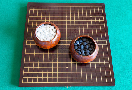 白色和黑的顶部观赏着绿桌上木板碗中的Go游戏玩石图片