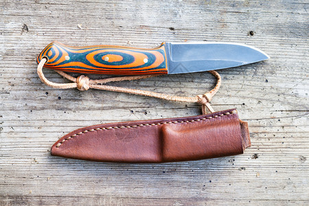 手工艺的黑色钢刀上面有土制环氧和橙色织物旧木板上有手工缝制的皮层图片